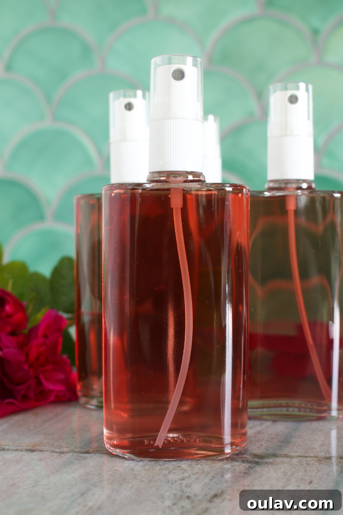Radiant Roses: DIY Simmered Facial Mist 8 Bottles of homemade rose water spray ready for use, alongside fresh rose petals.
