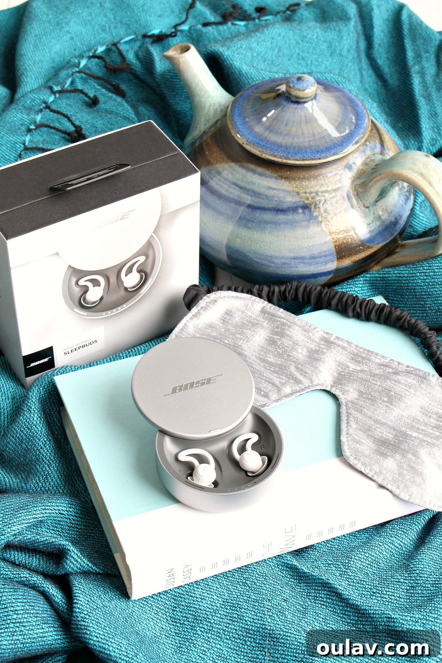 Holiday Haven: 25 Delightful Gifts for Homebodies 26 Bose Noise Masking Sleepbuds next to a silk eye mask on a soft surface, promoting restful sleep.