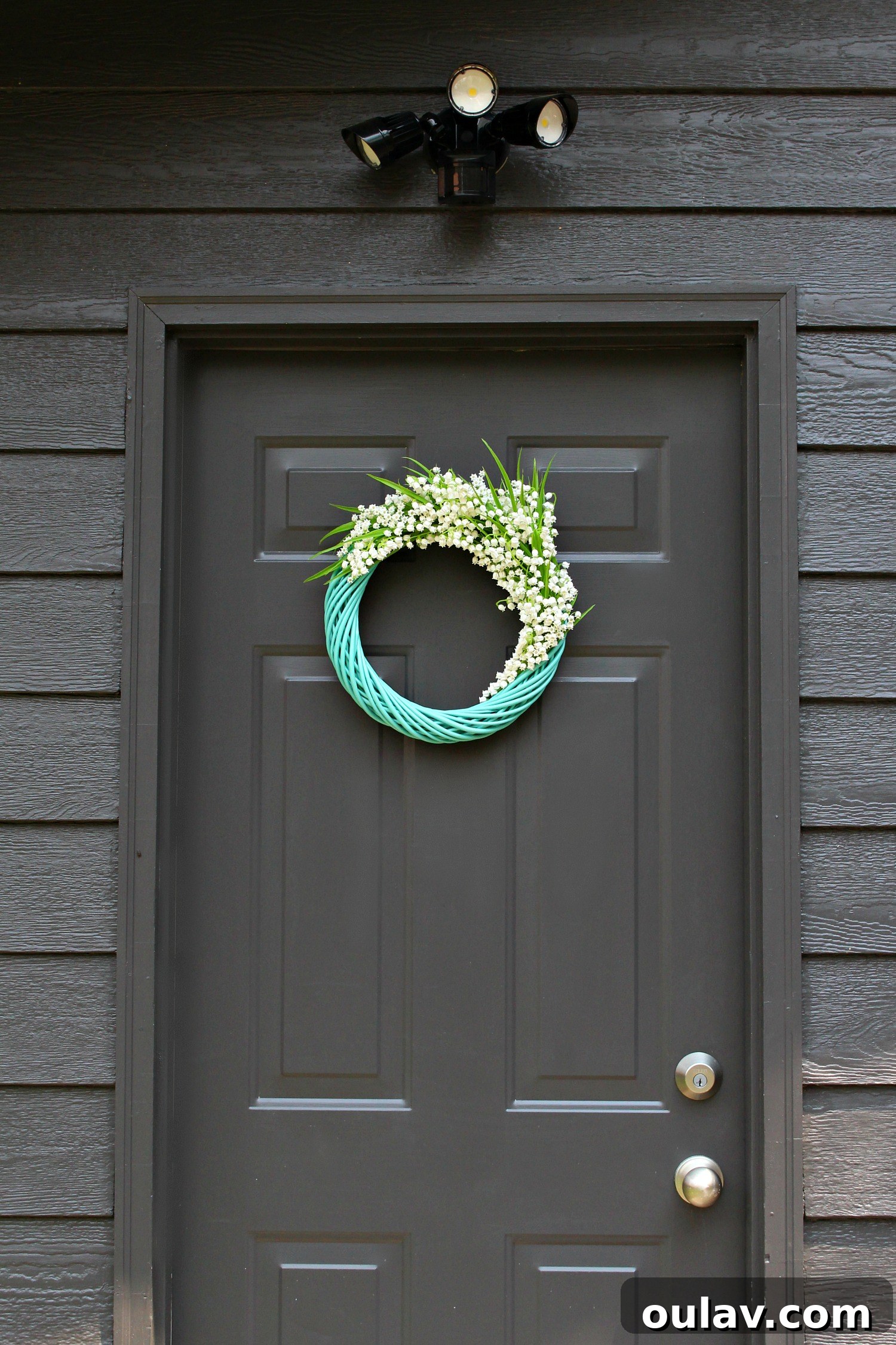Effortless Turquoise Lily Faux Wreath 17 Full view of the vibrant turquoise Lily of the Valley faux wreath on a dark door