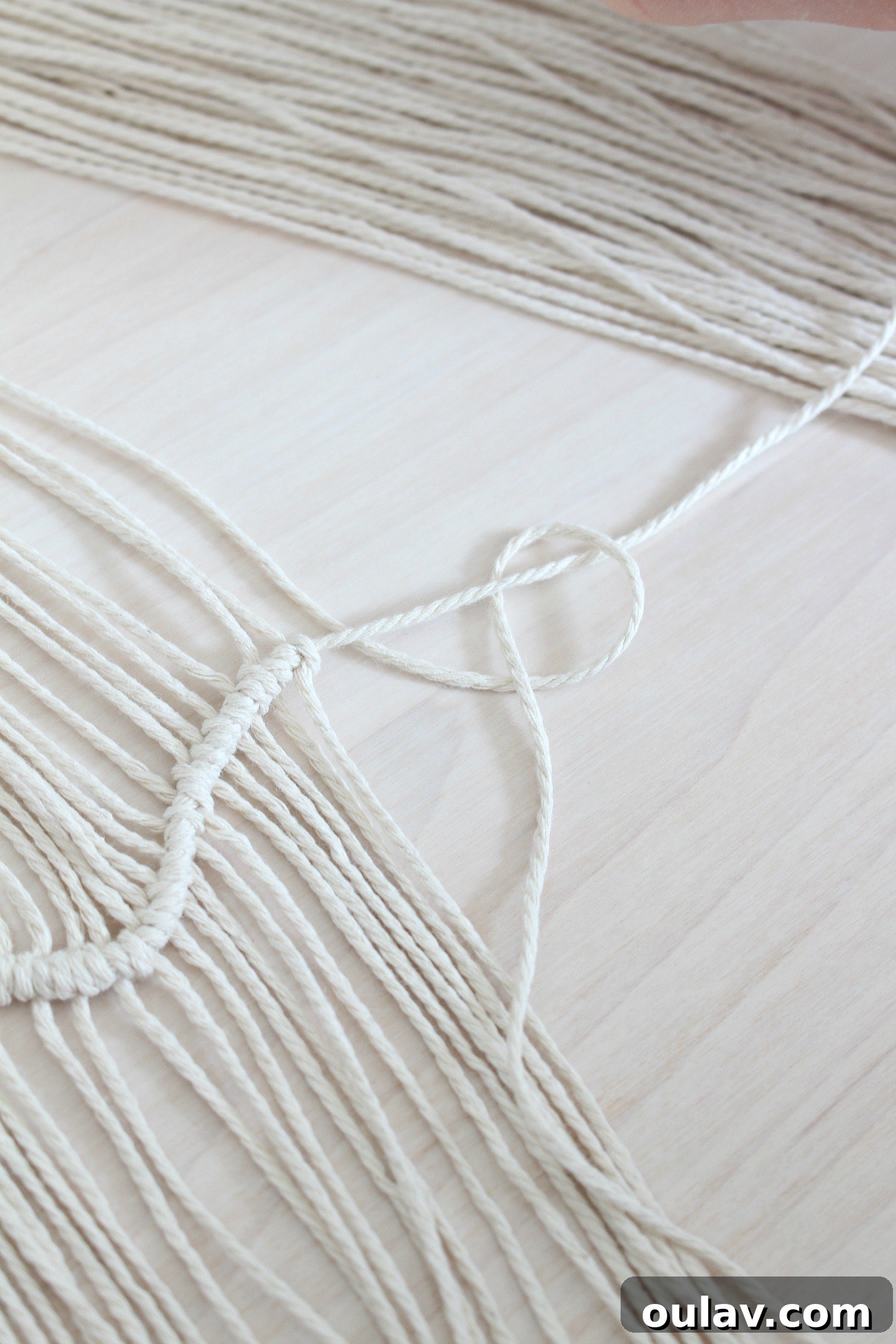 Handcraft Your Own Macrame Driftwood Wall Art 17 Close-up step-by-step photo showing the first stage of tying a clove hitch knot with the vertical string over the horizontal.
