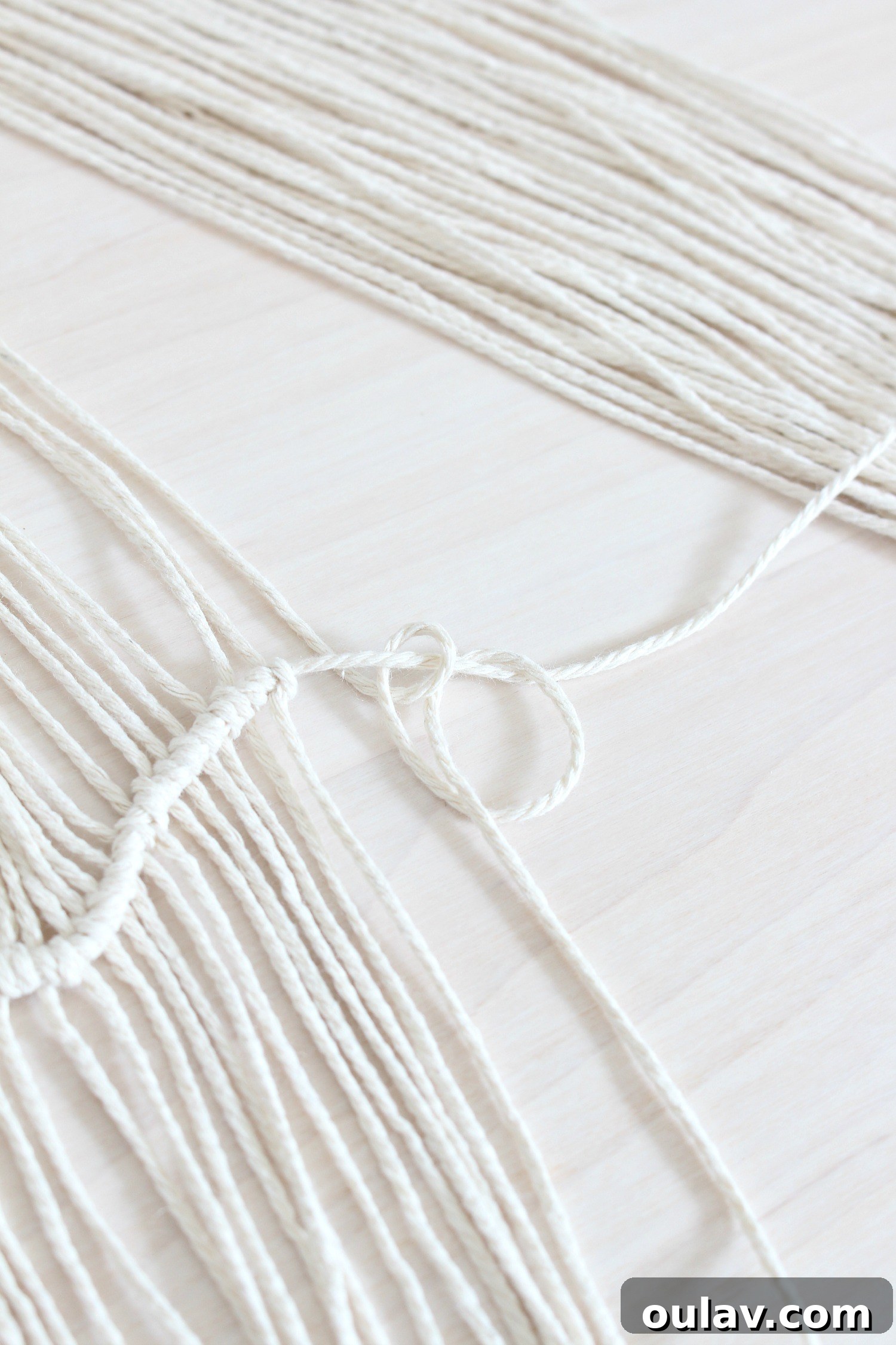 Handcraft Your Own Macrame Driftwood Wall Art 18 Second step of the clove hitch knot, showing the string being looped back over the horizontal piece and threaded through.