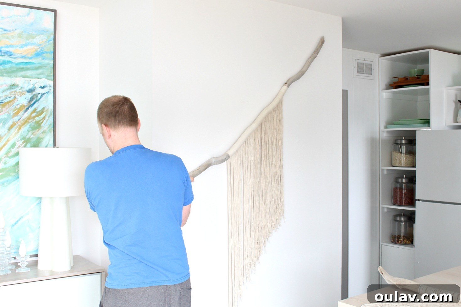 My husband holding up a large, unfinished macrame and driftwood wall hanging against a wall, showcasing its potential size.